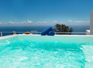 A pool with clear blue water, a blue towel, and a chair. - Santorini Heights (Santorini)