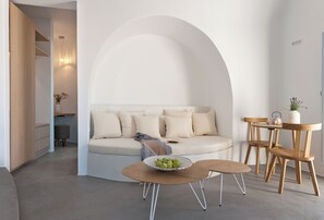 A modern living room with a sofa, a round wooden table with a bowl of fruit, and a small round table with a teapot. - Santorini Heights (Santorini)