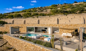 A modern villa with a swimming pool, outdoor seating, and a stone wall backdrop. - Santorini Heights (Santorini)