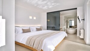 A modern bedroom with a large bed, a glass door leading to a bathroom, and a minimalist design. - Santorini Heights (Santorini)