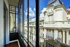 Uitzicht vanaf een balkon met glazen hekwerk op een historisch gebouw met versierde architectuur en een klokkentoren.