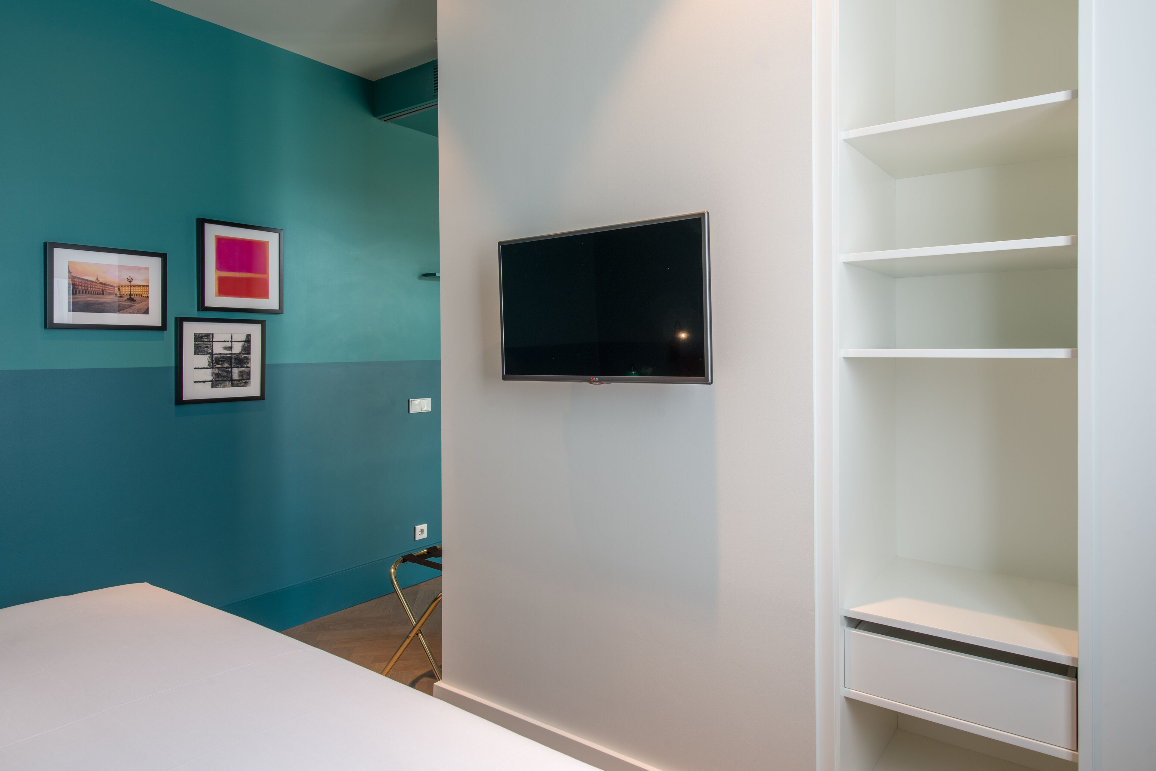 A room with teal and white walls, a flat-screen TV mounted on the wall, and a white shelving unit.