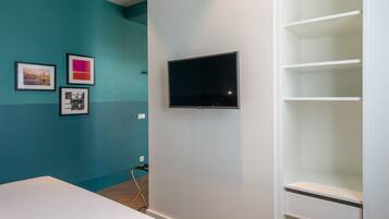 A room with teal and white walls, a flat-screen TV mounted on the wall, and a white shelving unit.