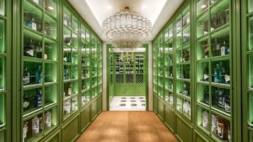 A green hallway with glass-fronted cabinets filled with bottles, leading to a room with a patterned floor.
