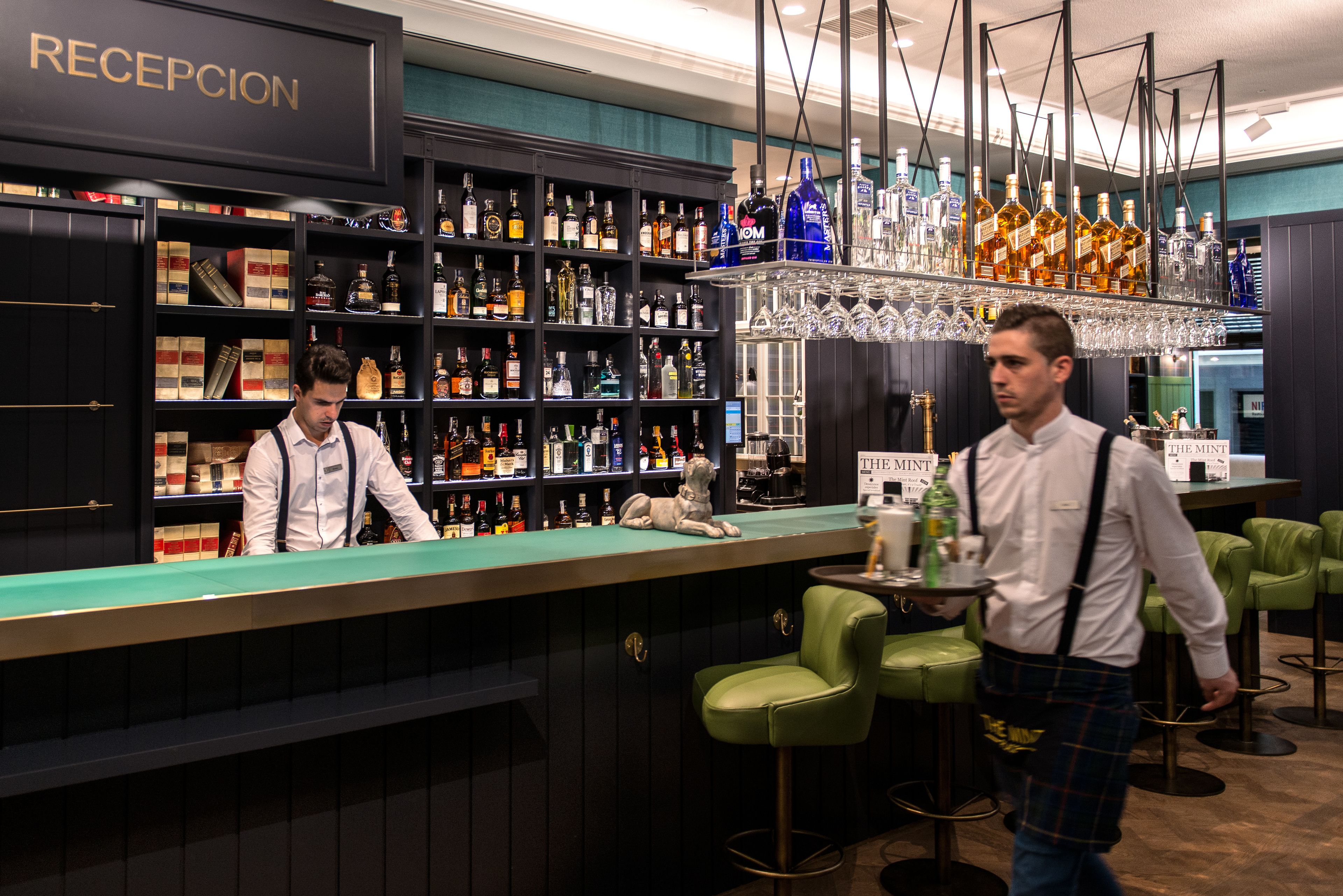 Un'area bar con scaffali pieni di bottiglie di liquori, una reception e sgabelli da bar verdi.
