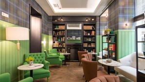 A cozy room with green upholstered chairs, a fireplace, and bookshelves filled with books. - Hotel Vincci The Mint (Madrid)