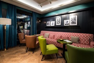 A modern lounge area with a red and white patterned sofa, green chairs, and a small round table.