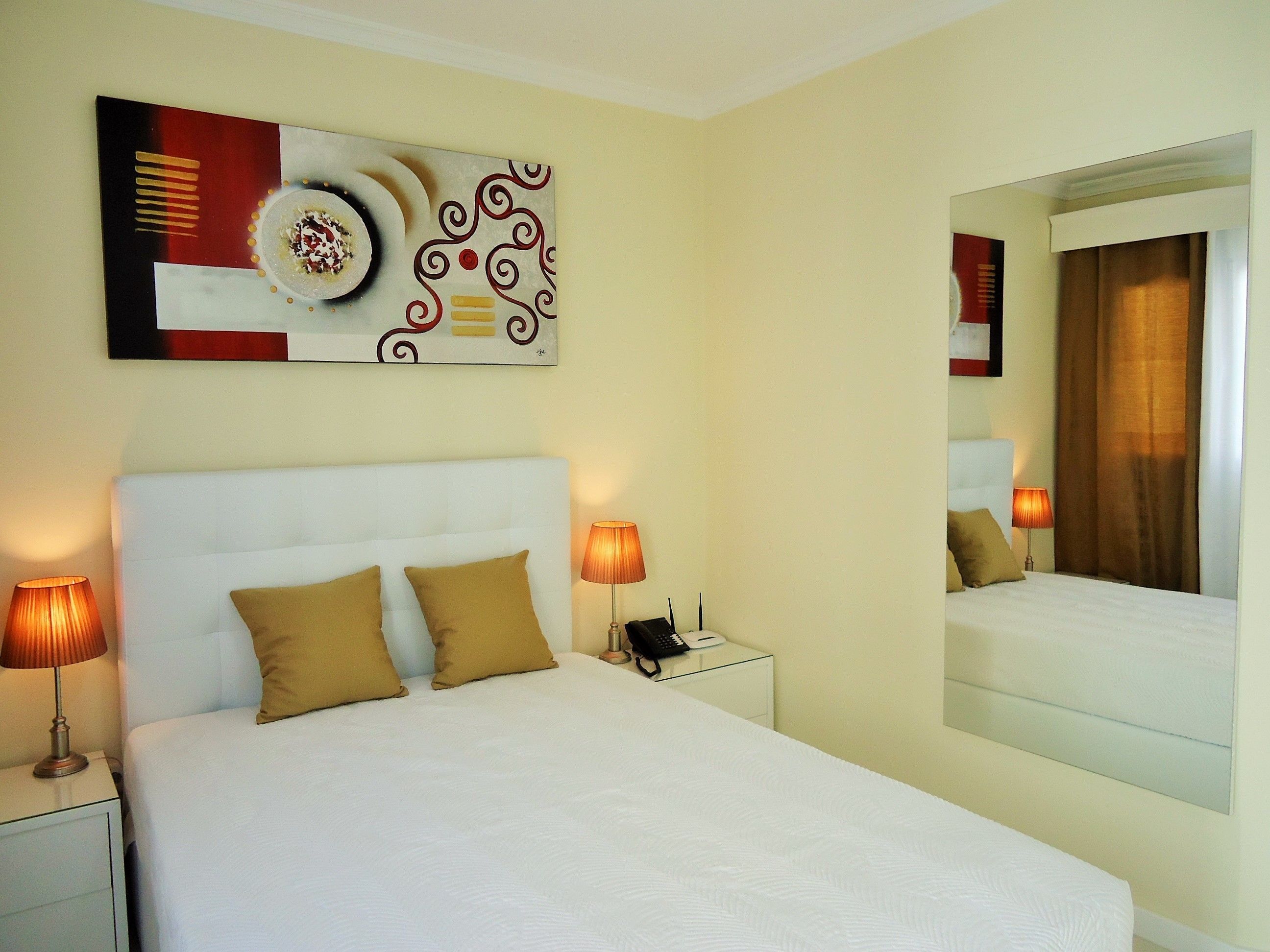 A hotel room with a large bed, two bedside lamps, a bedside telephone, and a wall-mounted mirror.
