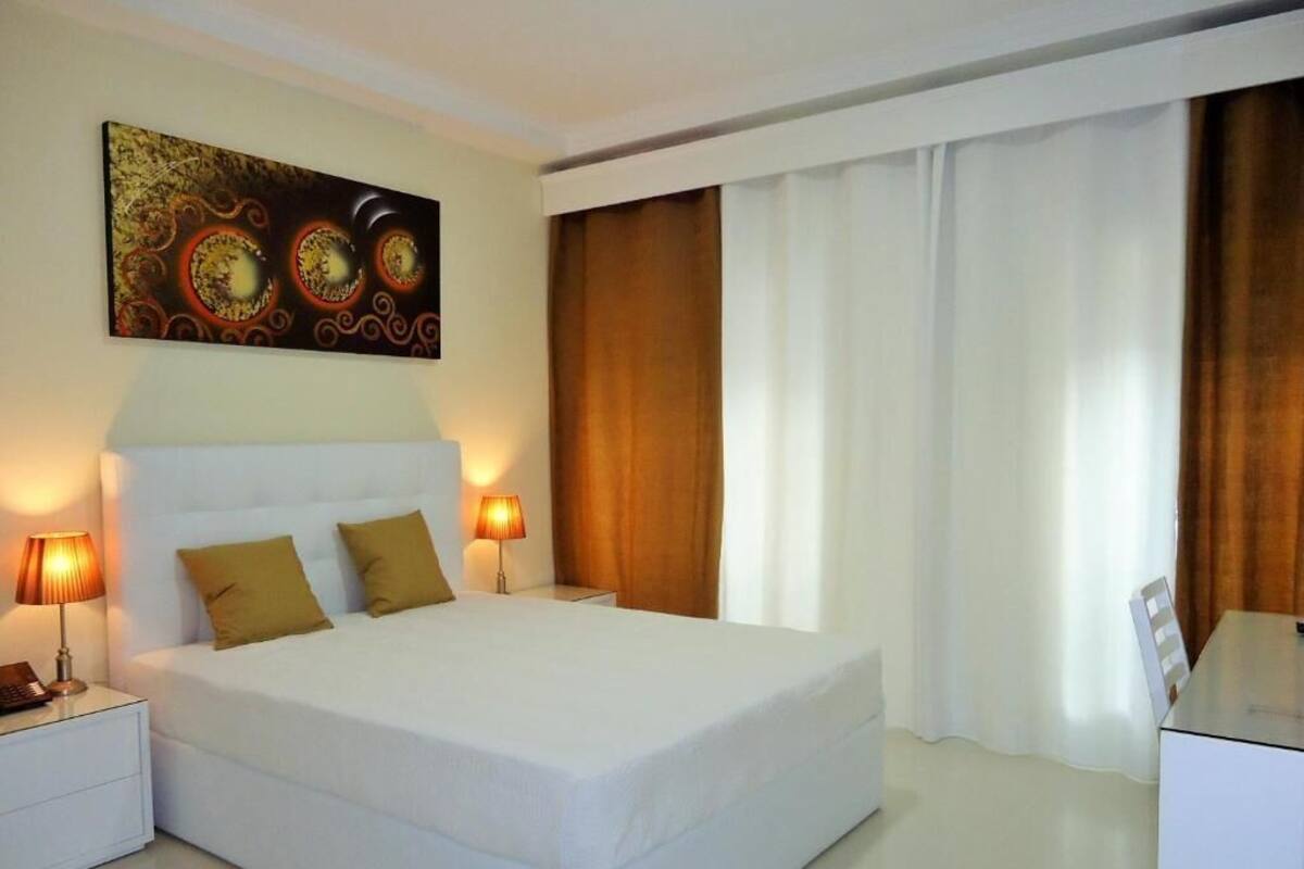 A neatly made bed with two pillows, a bedside lamp, and a painting above it.