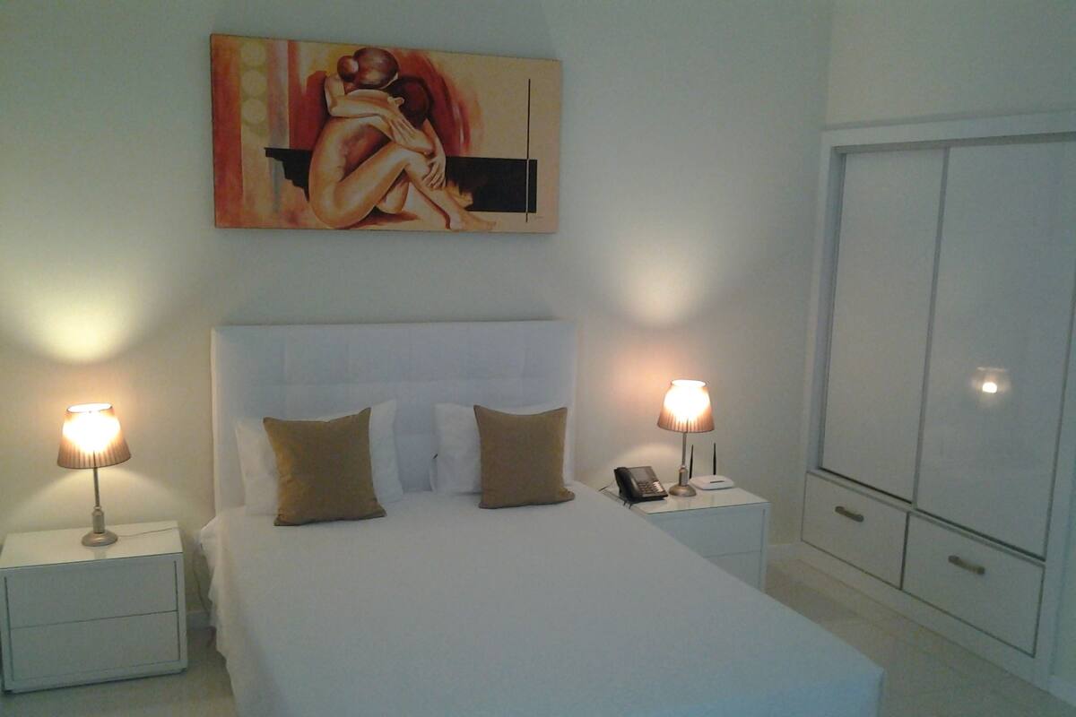 A hotel room with a large bed, two bedside tables, a nightstand, a telephone, a lamp, and a wardrobe.