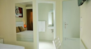 Une chambre d’hôtel comprenant un lit, une lampe de chevet, une salle de bain avec un lavabo et un miroir, et une douche.
