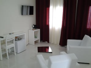 A modern living room with white furniture, a flat-screen TV mounted on the wall, and a window with red curtains.