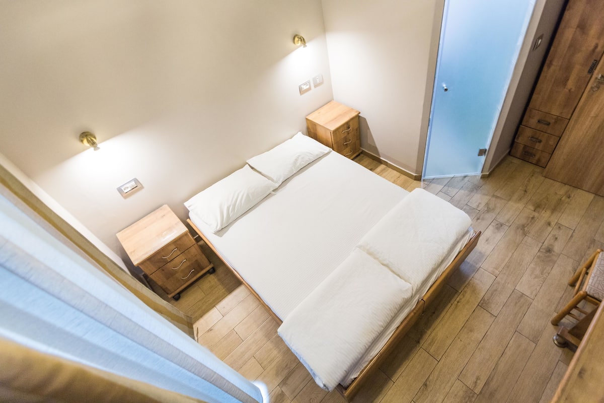 Un dormitorio con una cama grande, mesitas de noche de madera y un armario.