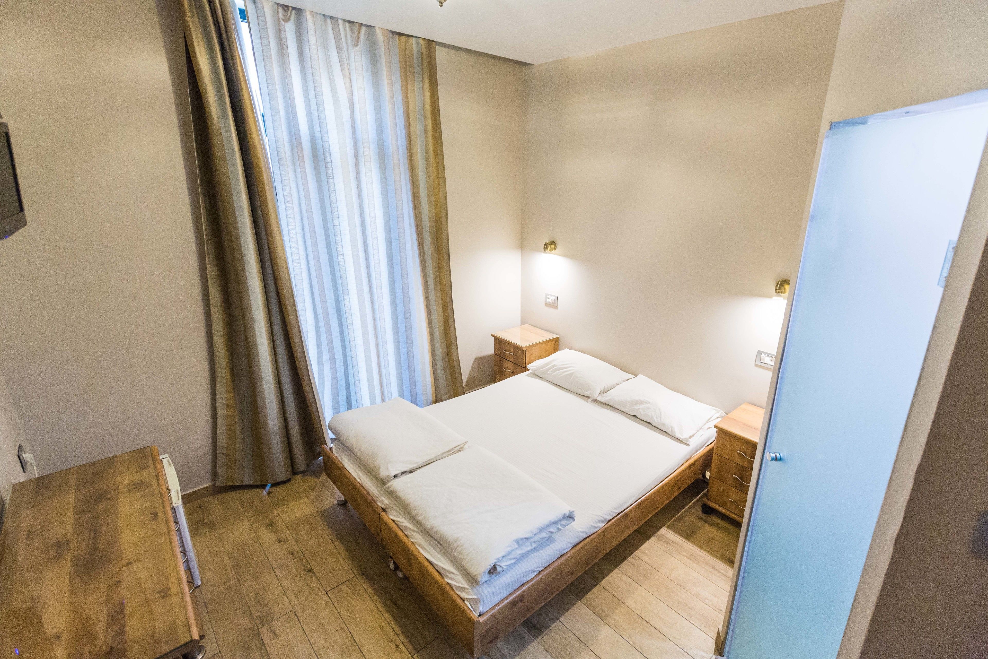 A neatly made bed with white linens, a wooden nightstand with a lamp, and a blue door.