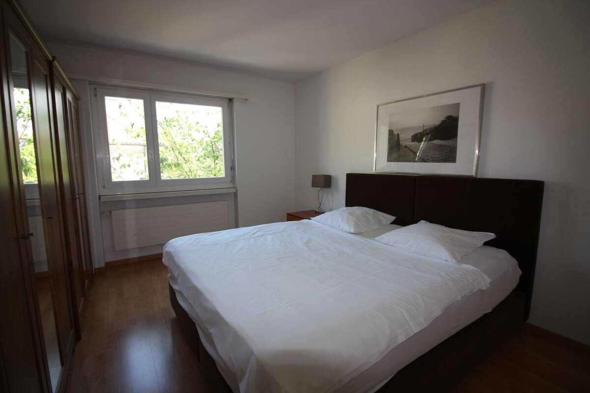 A bedroom with a large bed, a window, a bedside table, and a framed picture on the wall.