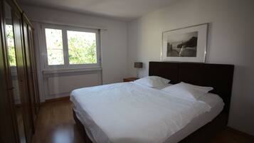 Une chambre avec un grand lit, une fenêtre, une table de chevet et un tableau encadré au mur.