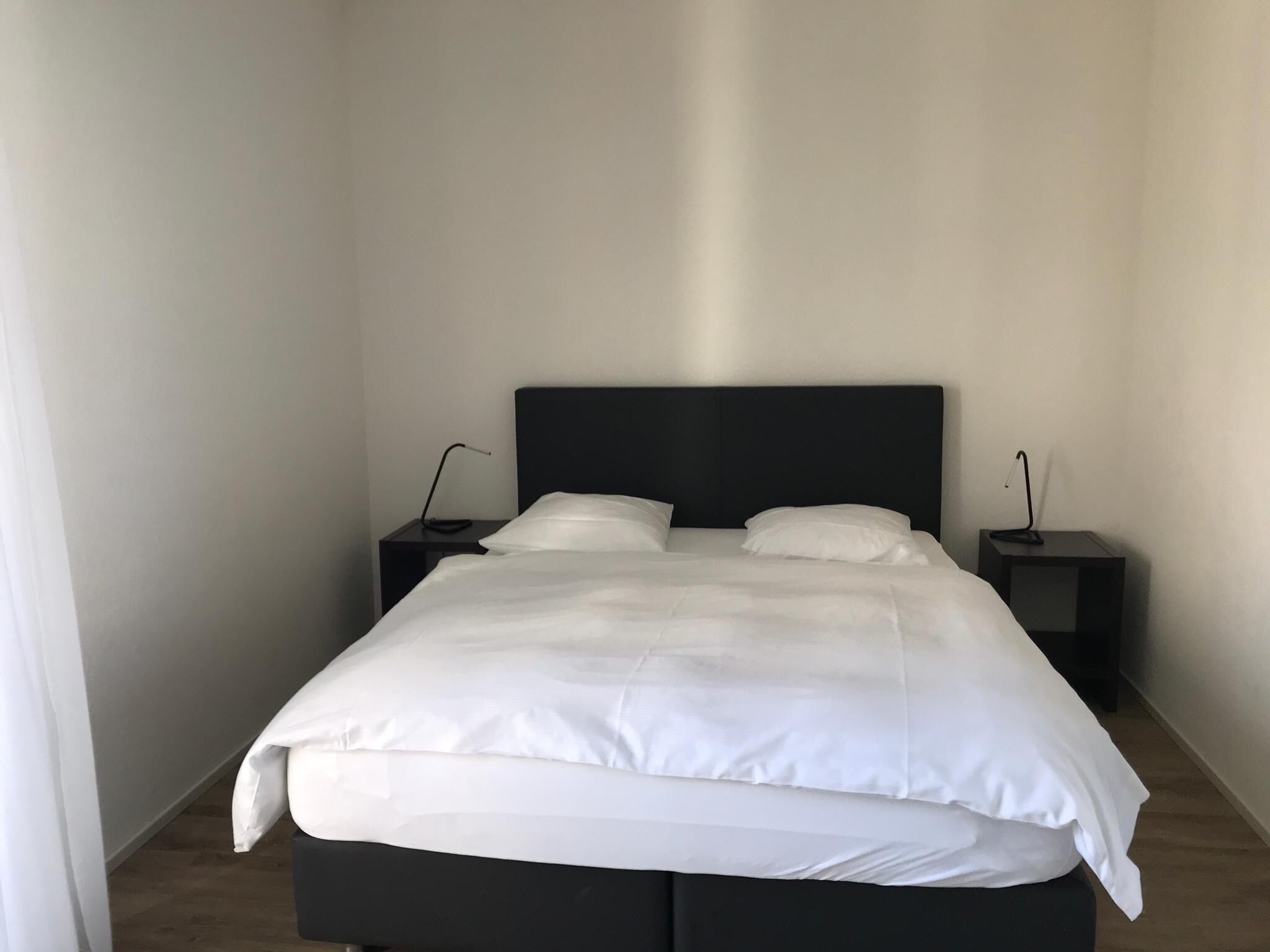Een minimalistische slaapkamer met een groot bed, twee nachtkastjes en een effen muur.