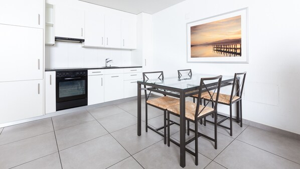 A modern kitchen with white cabinets, a black oven, and a dining table with four chairs. - Swiss Star Wiedikon (Zürich)
