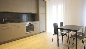 Cozinha moderna com armários cinza, forno embutido e área de refeições com mesa e cadeiras.