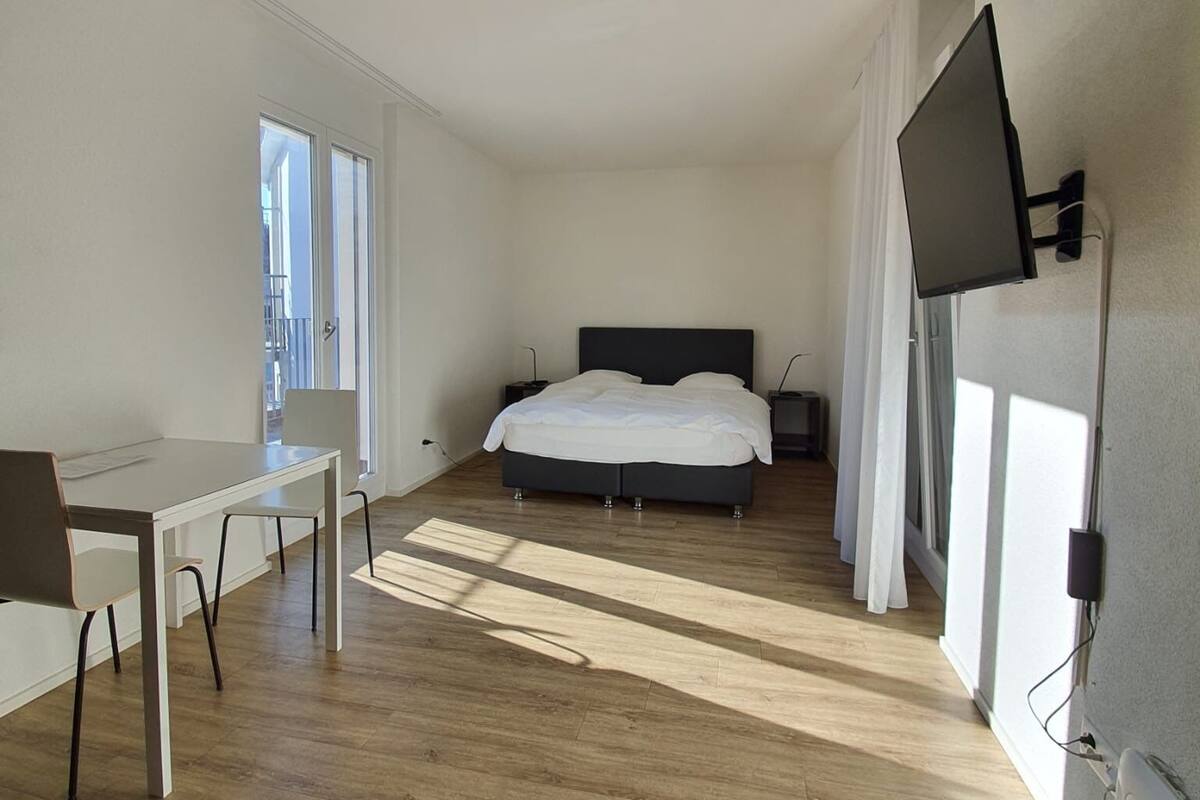 A modern bedroom with a bed, a desk, and a TV.