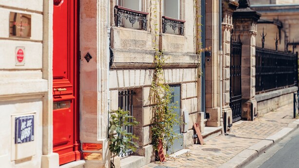 A historic building with a red door, stone facade, and a cobblestone street. - Le Clos d'Emile (Bordeaux)
