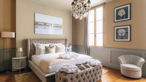 A bedroom with a large bed, a chandelier, a chair, and artwork on the walls. - Le Clos d'Emile (Bordeaux)