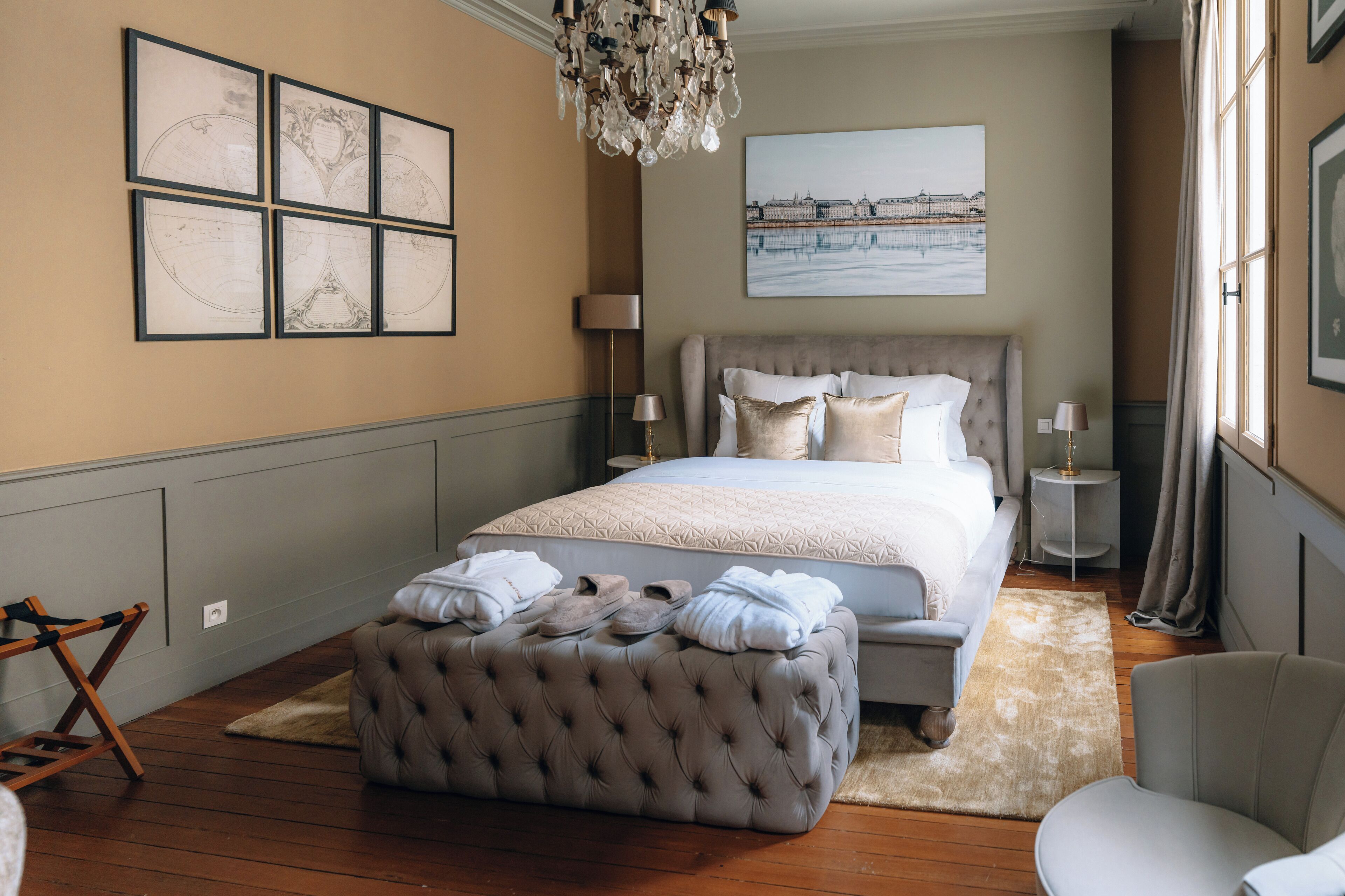 Een slaapkamer met een groot bed, een knopenbankje, een stoel en kunstwerken aan de muur.