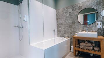 A modern bathroom with a glass-enclosed shower, a white bathtub, a wooden vanity with a sink, and patterned tiles on the walls.