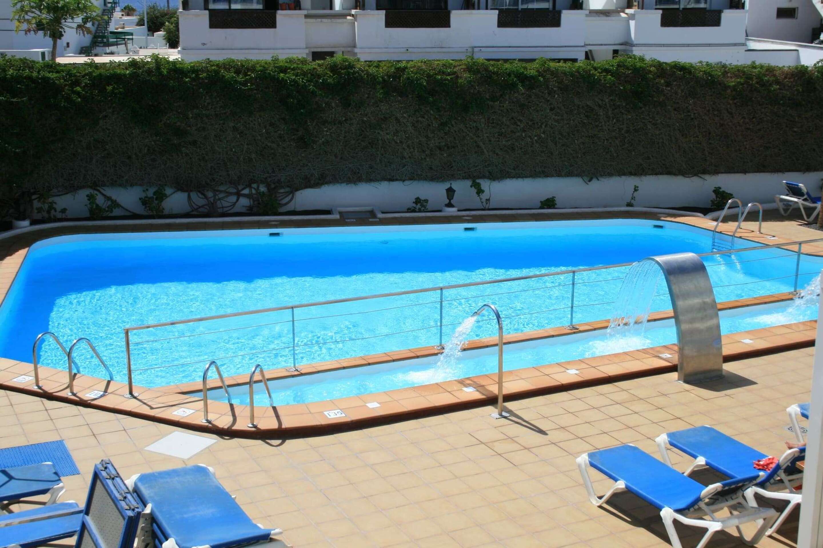 Una piscina al aire libre, sombrillas, sillones reclinables de piscina