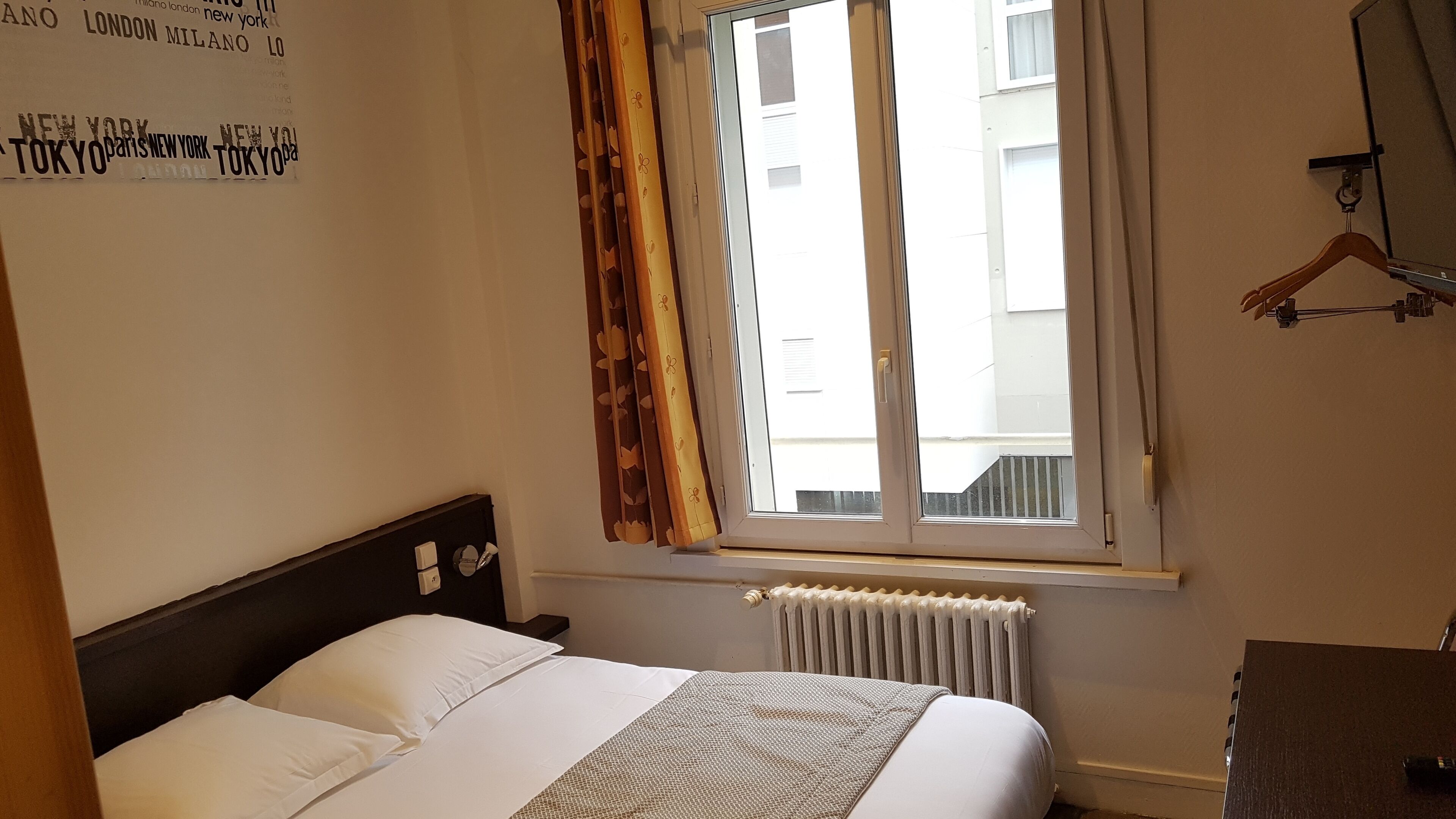 A hotel room with a bed, a radiator, and a window with curtains.