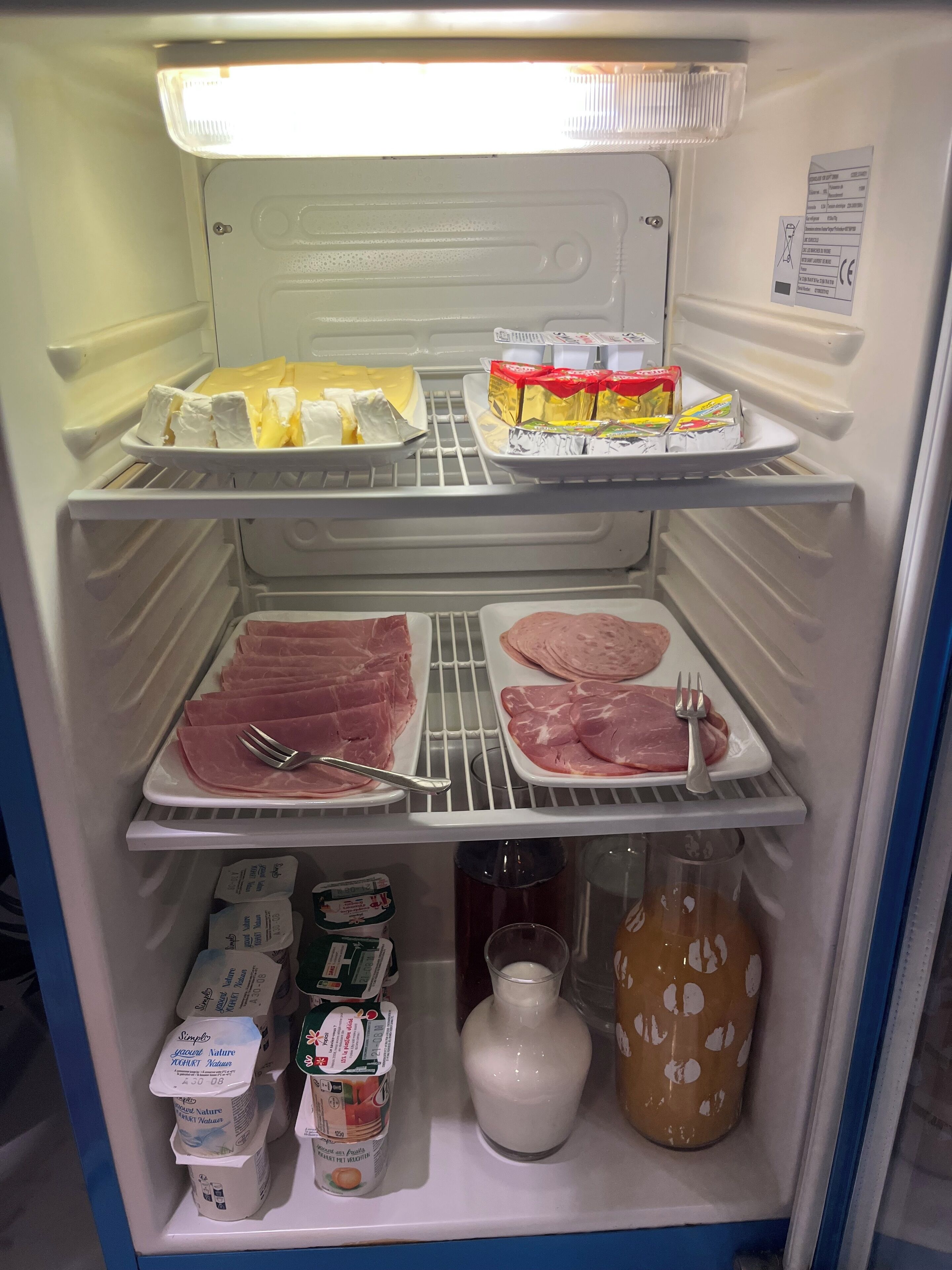 Ein Kühlschrank mit Regalen, auf denen verschiedene Lebensmittel liegen, darunter Käse, verpackte Waren und rohes Fleisch.