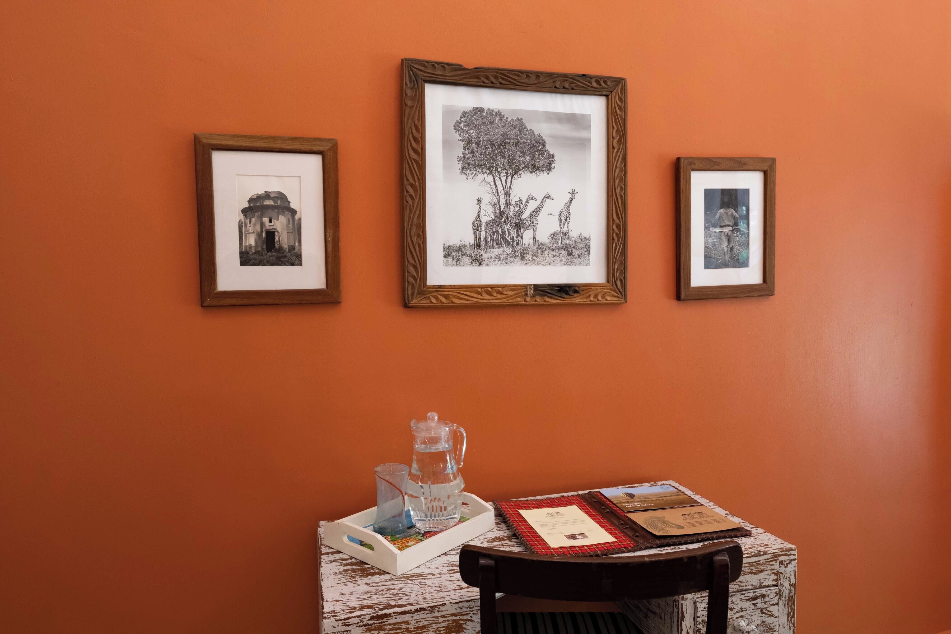 A room with a table displaying framed photographs on the wall, a pitcher, and a tray with glasses.