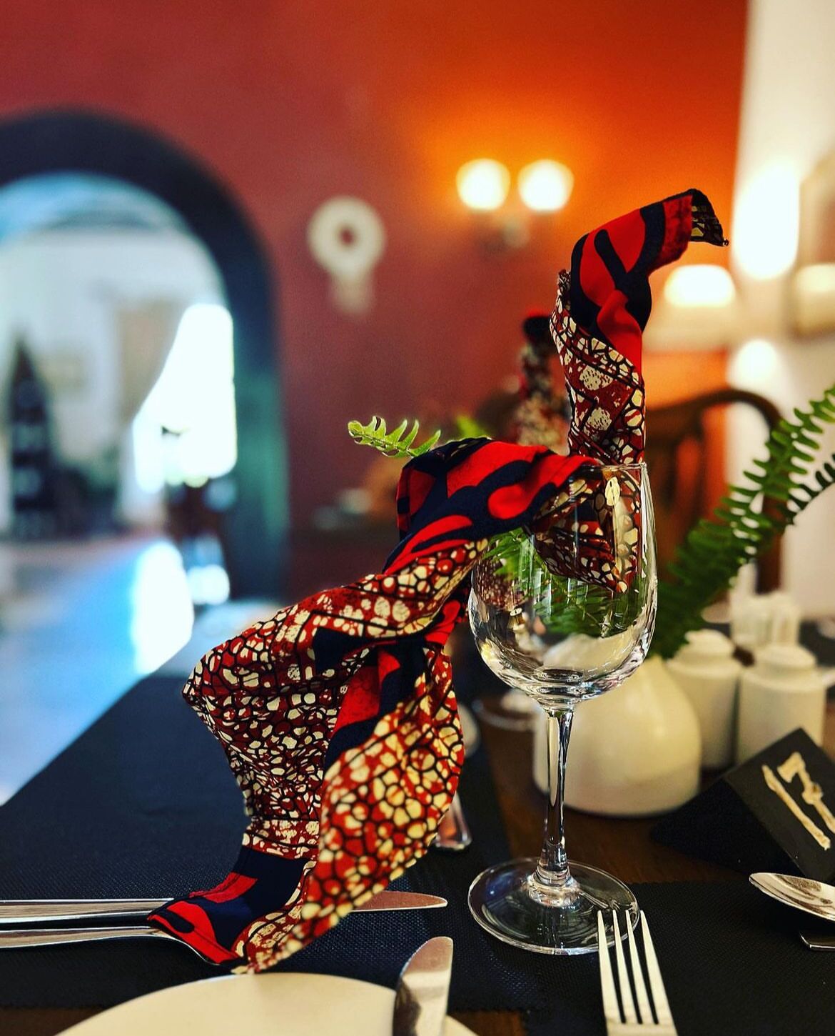 Una mesa de comedor con un centro de mesa de cristal, un servilleta estampada y un menú.