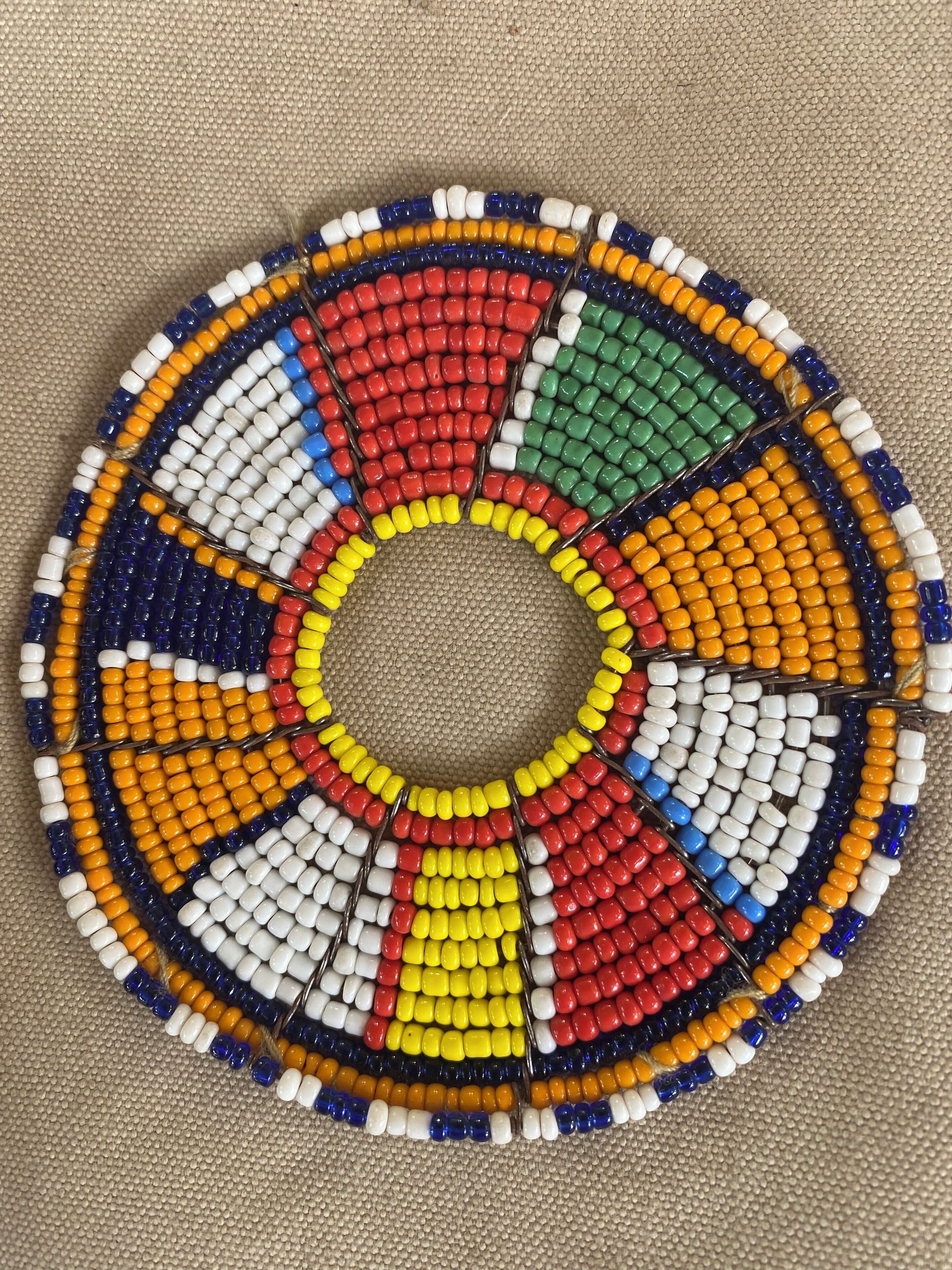 A circular beaded artwork with a central hole, featuring a variety of bead colors arranged in a radial pattern.