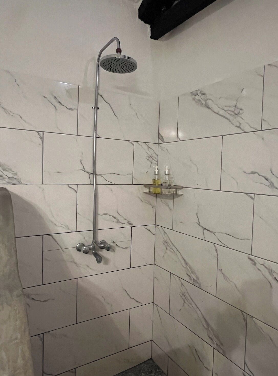 A shower with a handheld showerhead, a wall-mounted faucet, and a soap dispenser on a shelf.