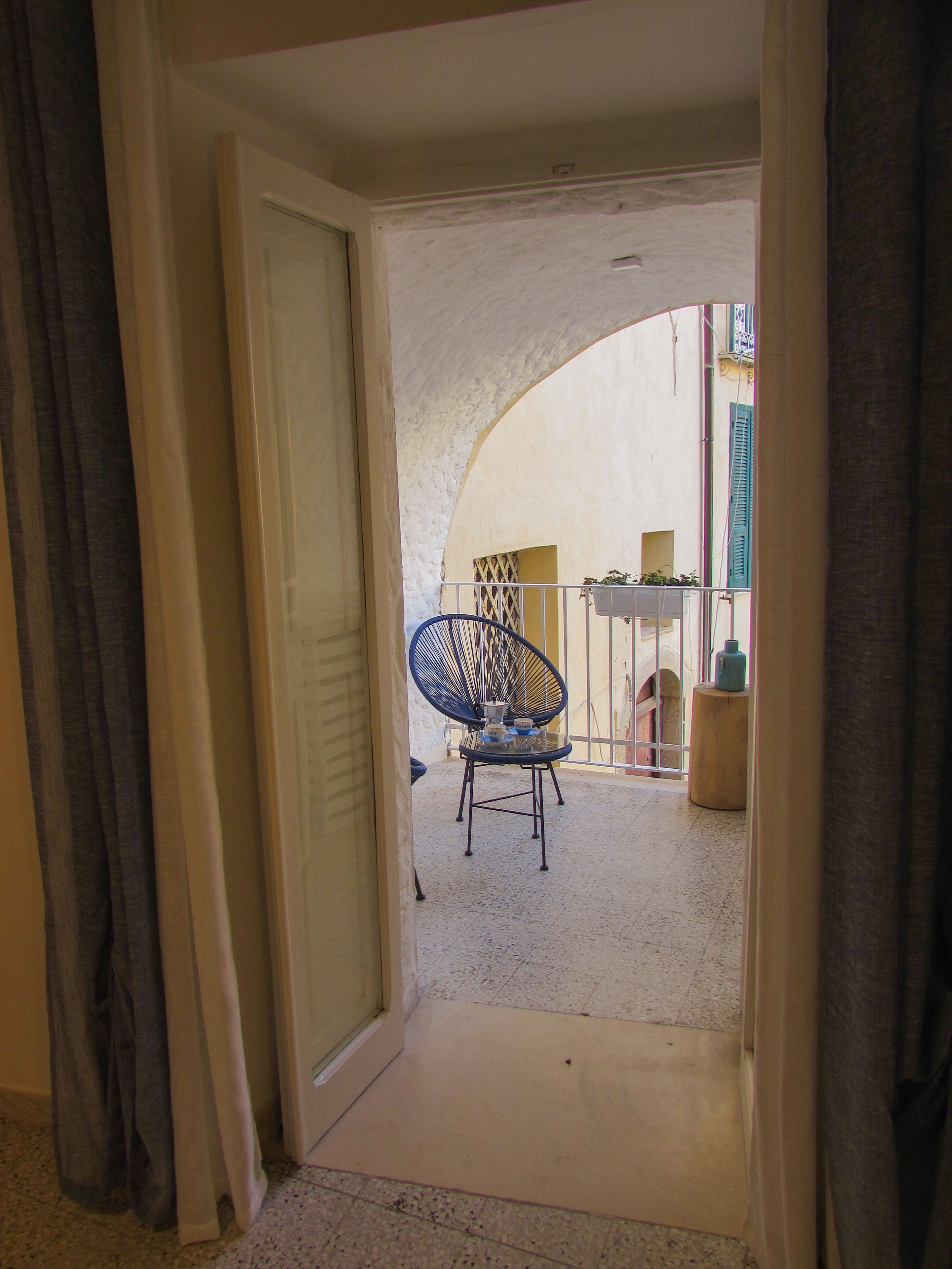 An interior corridor leading to a balcony with a chair and a table.