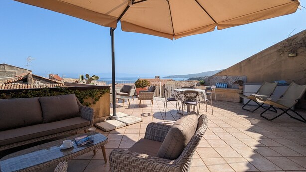 A terrace with wicker furniture, a table with a cup and magazine, and a view of the sea.