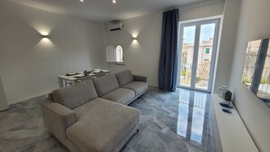 A modern living room with a grey sectional sofa, a dining table set for four, and a large sliding glass door leading to a balcony.