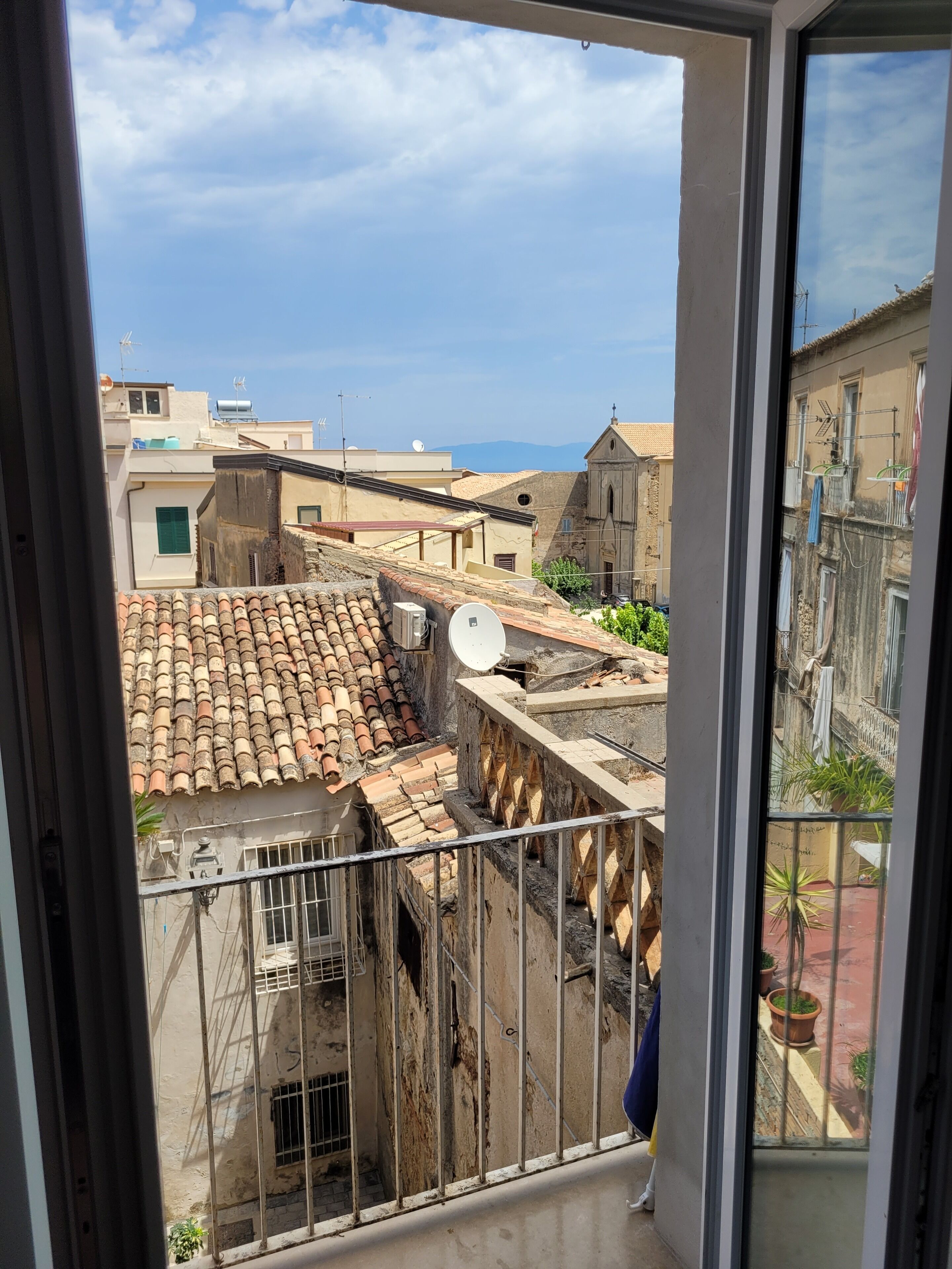 A view from a balcony overlooking a residential area with terracotta-tiled rooftops, satellite dishes, and a clear sky.