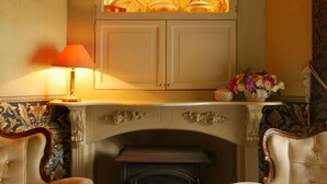 Un salón tradicional con chimenea, dos sillones, un aparador con objetos decorativos y una lámpara.