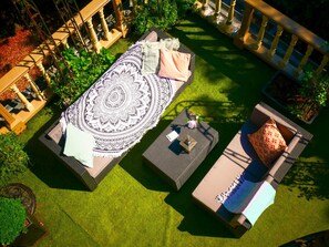 Un área de estar al aire libre con un tapete estampado, dos sillones acolchados y una mesita con un libro y una taza.