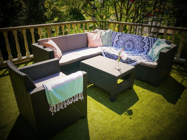 Een terras met rieten meubels, waaronder een bank en stoelen, en een bijzettafeltje.