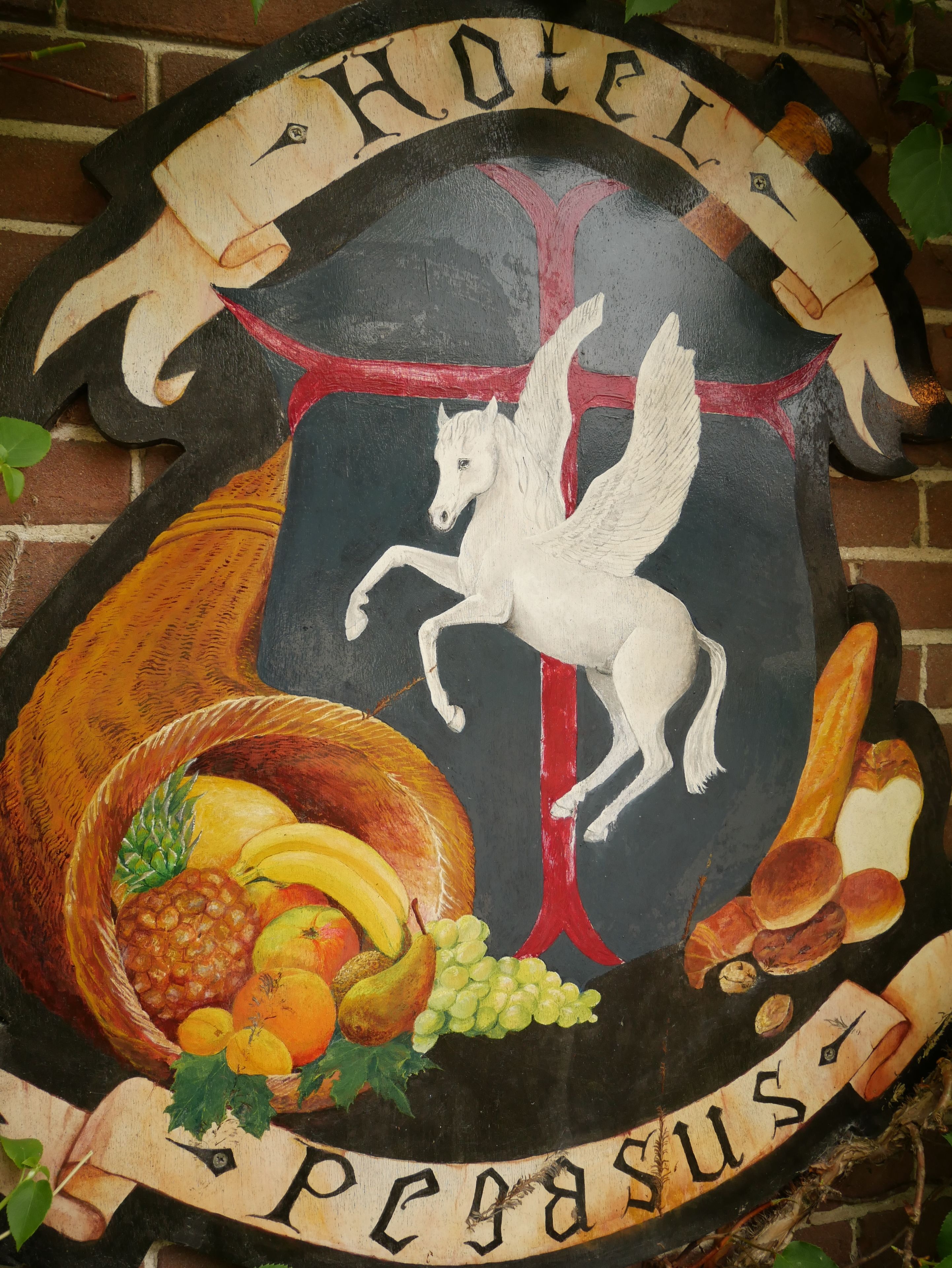 A hotel sign with a coat of arms, a white horse, and a fruit basket.