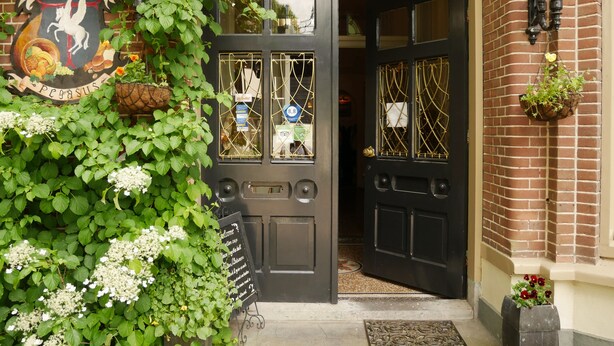 Una puerta negra con un letrero que dice "Hotel", una ventana con un cartel de "Zover" y un muro de ladrillo con plantas colgantes.