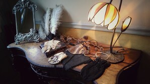 Un tocador de madera con un espejo, una lámpara y varios objetos decorativos, incluyendo un bolso tejido y una caja pequeña.