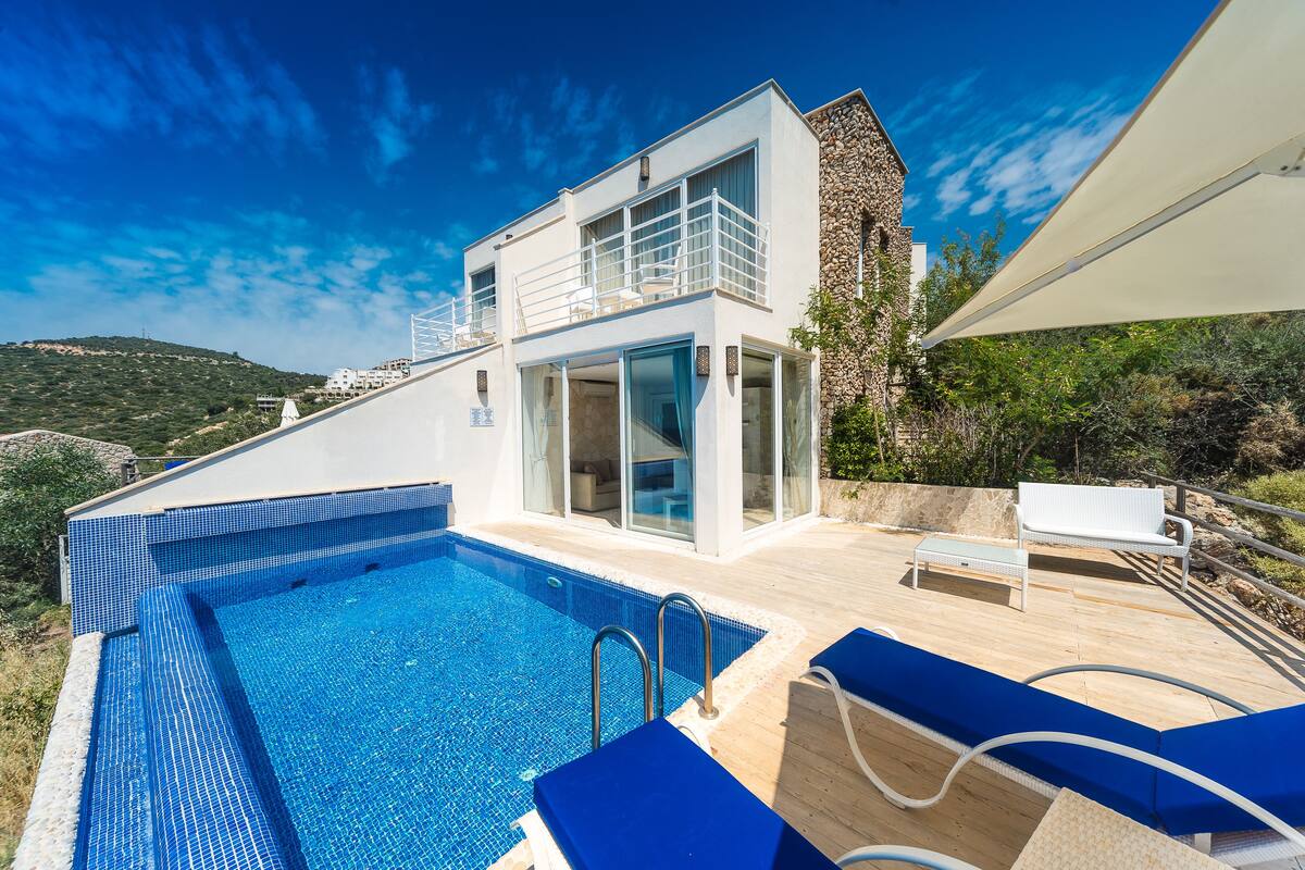 A modern villa with a swimming pool, outdoor seating, and a view of the surrounding landscape.