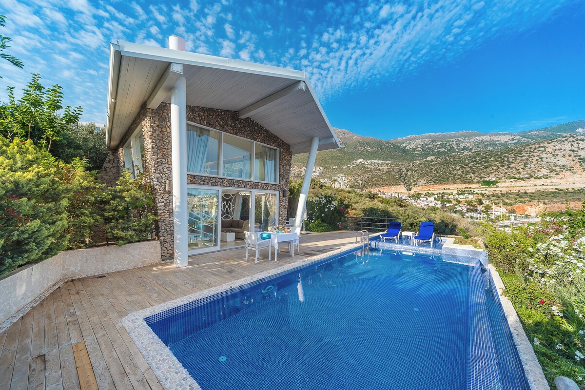 A modern house with a swimming pool, stone facade, and a view of the countryside.