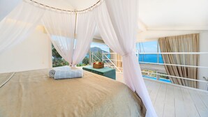 Een slaapkamer met een bed, nachtkastje en uitzicht op zee.