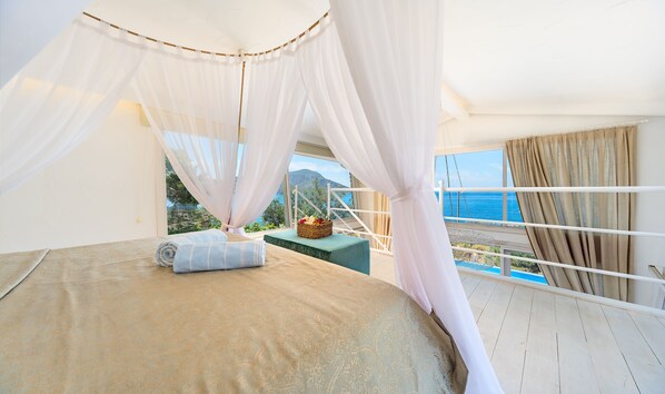 A bedroom with a bed, a bedside table, and a view of the sea.