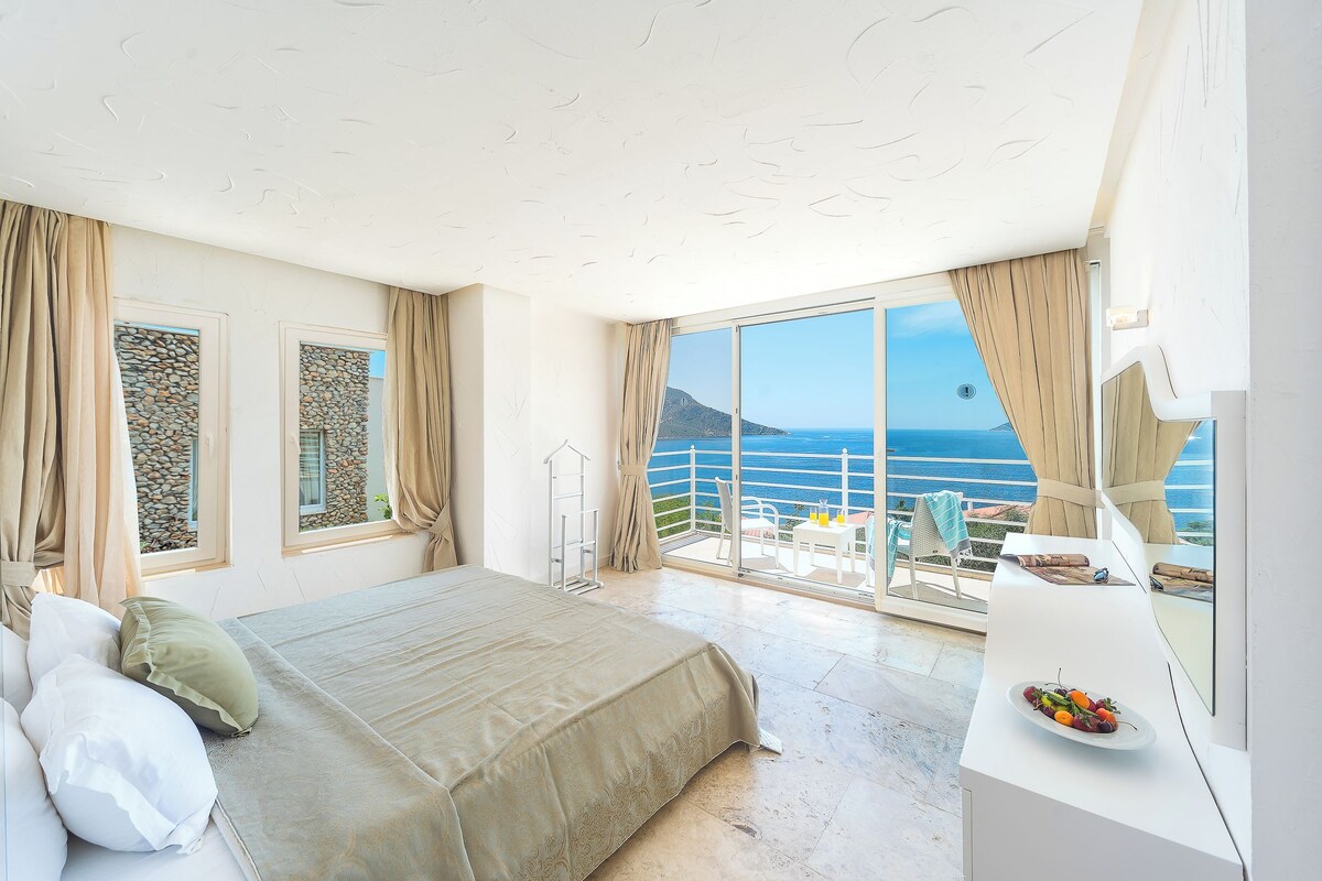 Ein Schlafzimmer mit Bett, einem Balkon mit Tisch und Stühlen sowie Meerblick.
